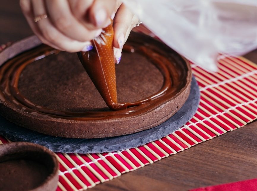 A chocolate cake being carefully iced.