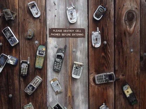 Image, old cell phones nailed to a door, with a sign saying 'Please destroy cell phones before entering'. 