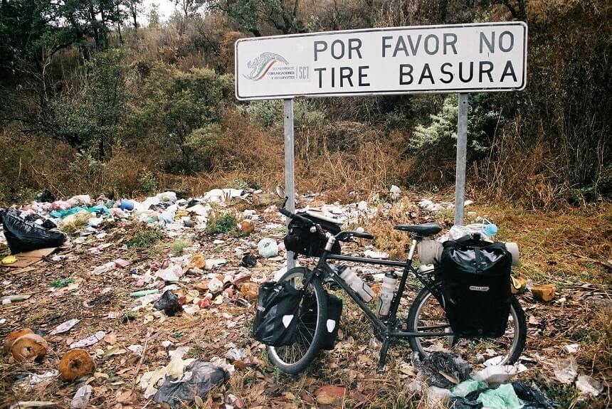 Image, pushbike leaning against a sign saying 'please do not litter', that's surrounded by rubbish