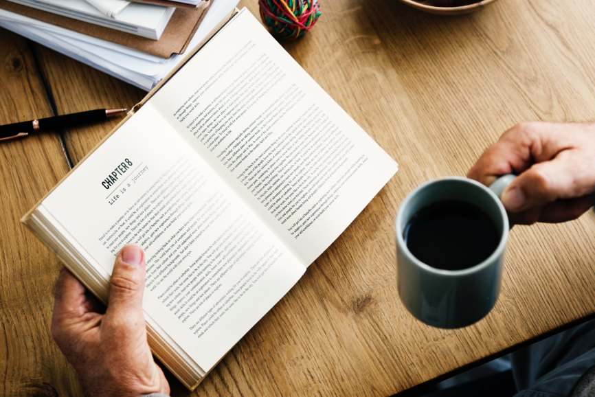 Photo of hands holding an open book and a mug of coffee.