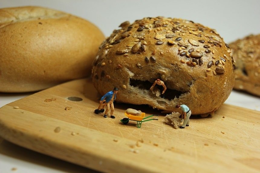 Miniature landscape of three tiny model humans and a wheelbarrow mining the insides of a bread roll