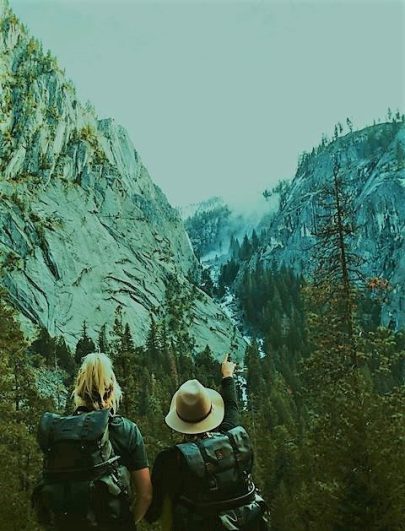 Image, two mountain climbers overlooking a mountain valley and pointing to a waterfall.