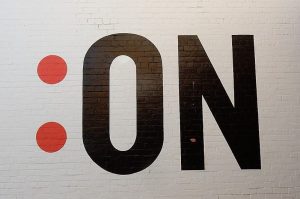 Image of a colon and the word 'on' painted on a brick wall.