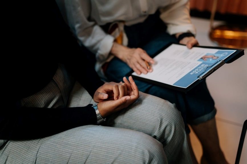 Person holding a clipboard with a resume on it talking to the person beside them