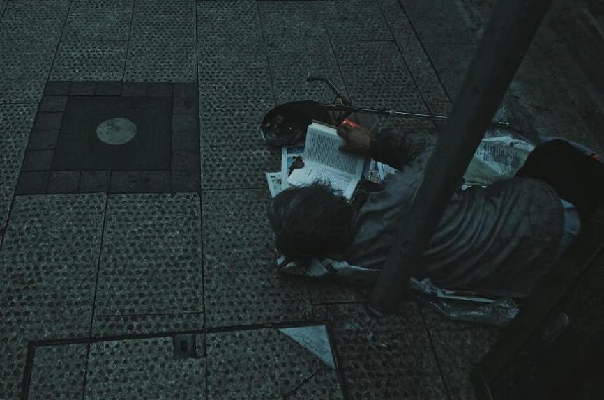 Image, homeless person reading a book on a nest of newspapers