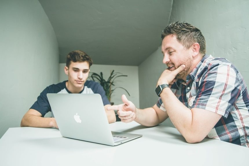 Two men discussing something on a laptop screen. 