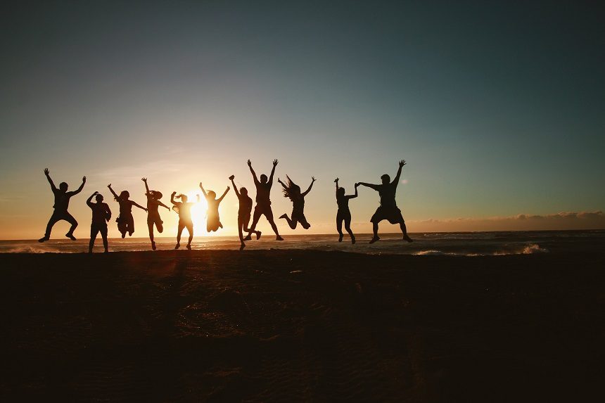 Image, a group of people leaping into the air on a beach at sunset