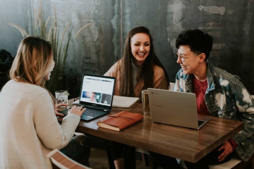 Group of people laughing together while they work sitting at a table with laptops