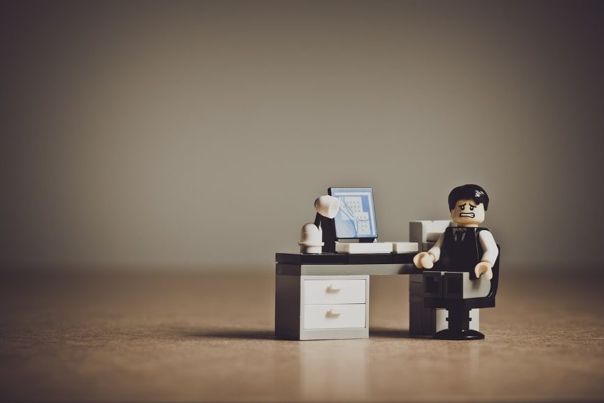 A small Lego man figurine sitting at a desk looking frustrated.