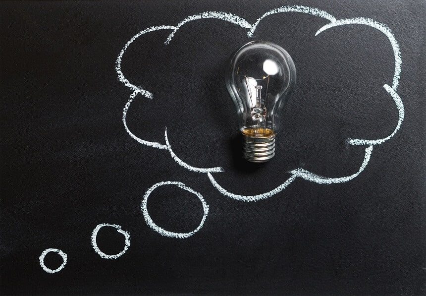 Image, glass lightbulb against an ideas cloud that's been drawn on a blackboard