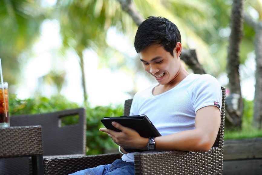 A young man looks at his tablet with a smile.