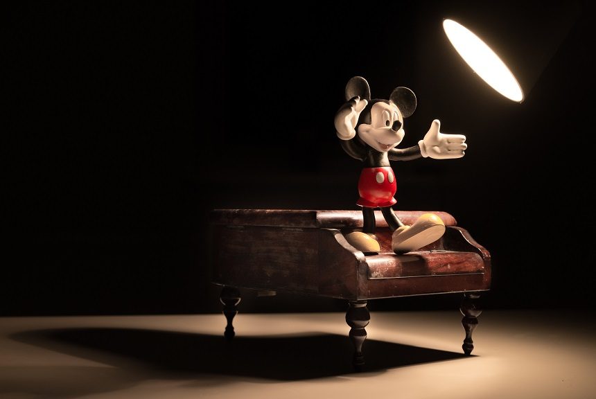 Smiling Mickey Mouse dancing on a piano, lit by a spotlight.