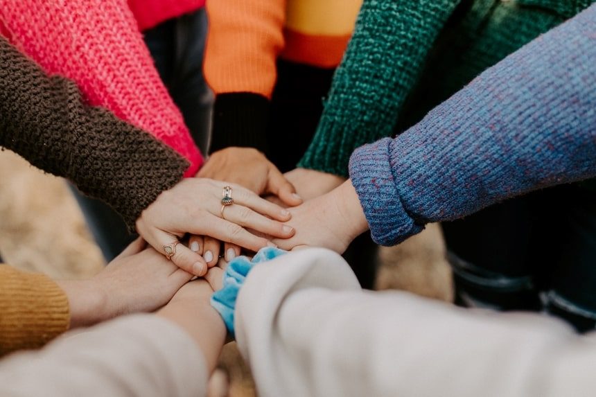 People putting their hands on top of each other in a team work circle. 