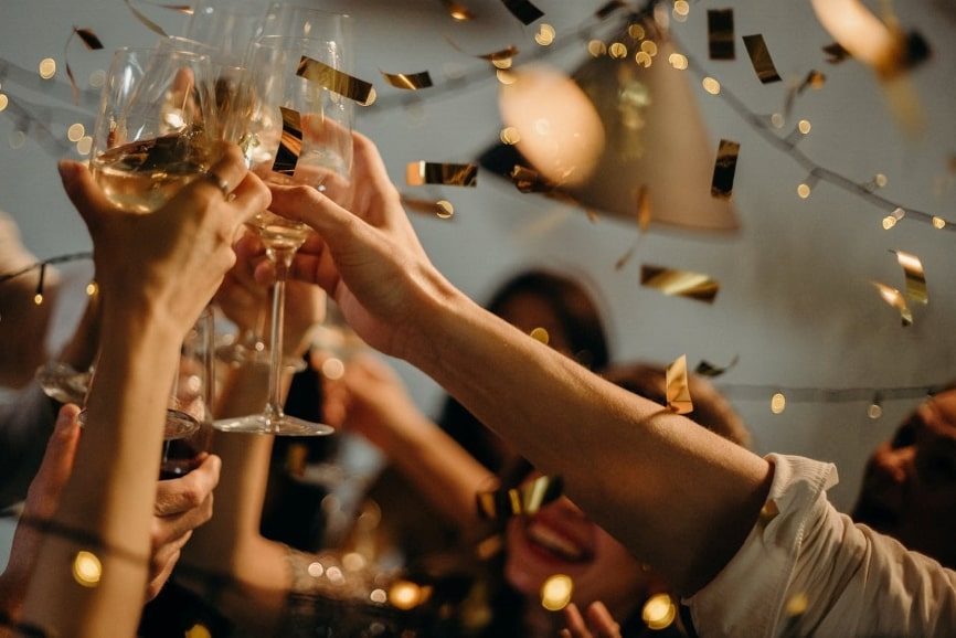 People toasting wine glasses with golden confetti and golden streamers falling around them