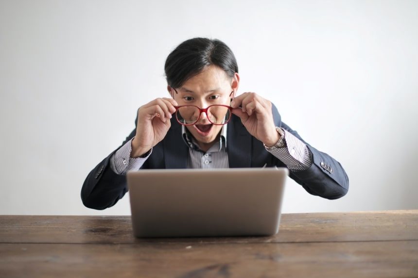 A man looking at a laptop. He’s surprised — his mouth is open, eyes are wide open, and he’s holding his glasses in front of his eyes a few centimetres (as if he can’t believe what he’s reading).