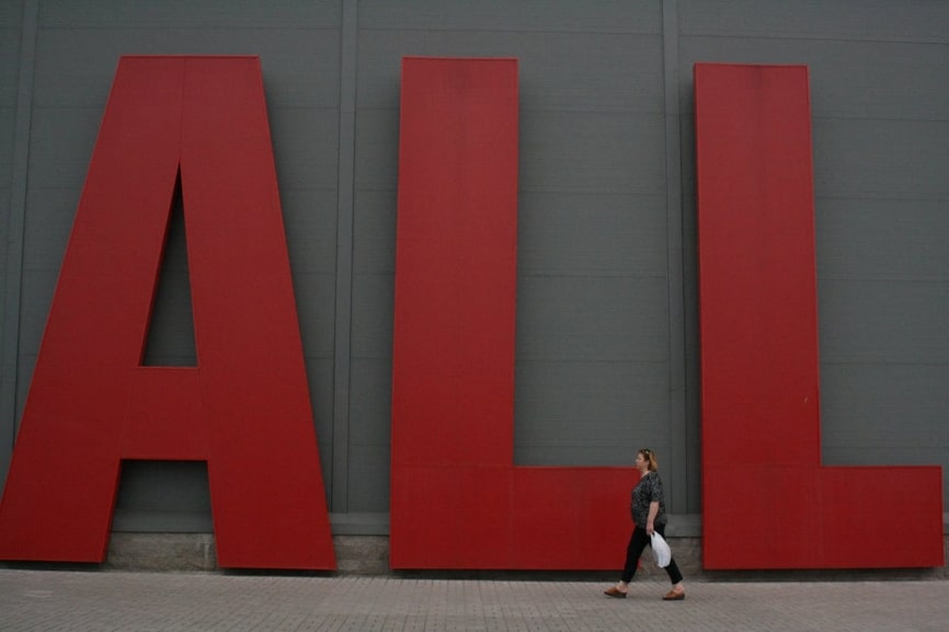 Woman walking on street under big red letters that spell all