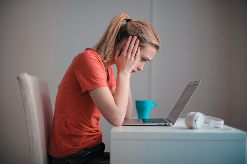 Image, woman sitting at a desk looking at her laptop in misery