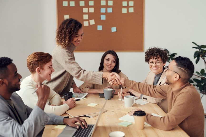 Colleagues shaking each other's hands across a desk. Learn how to write a proposal that seals the deal.