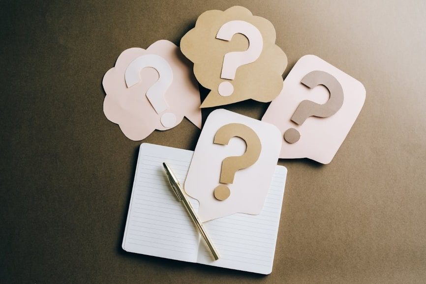 Question marks on craft paper and a pen lying next to them 