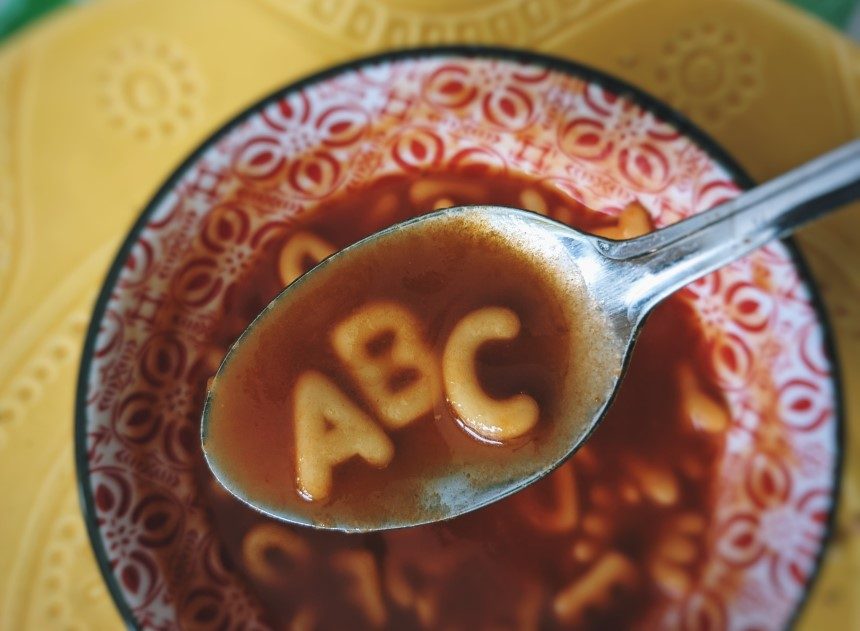 Bowl of soup with a spoon holding noodles shaped as A, B, C