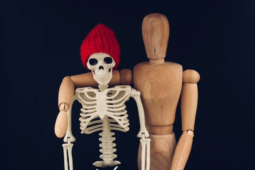 Wooden figure with arm around a skeleton wearing a red woolly hat.