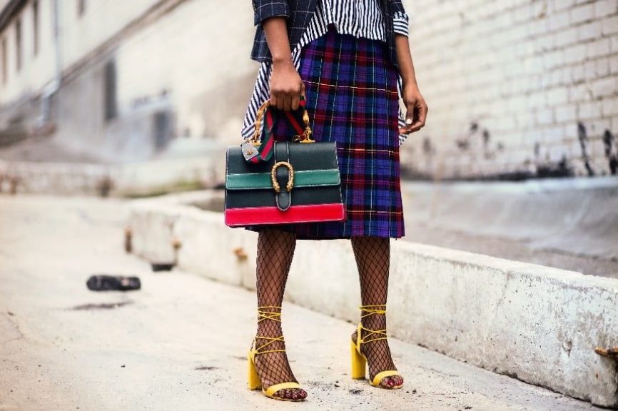 Image, Woman with yellow high heels, fishnet stockings, tartan skirt, stripy shirt, checked jacket, and stripy bag.