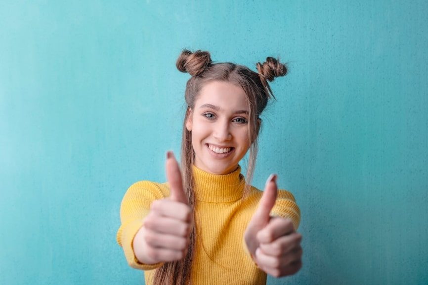 Woman in yellow turtleneck sweater smiling and giving a thumbs up with both hands 