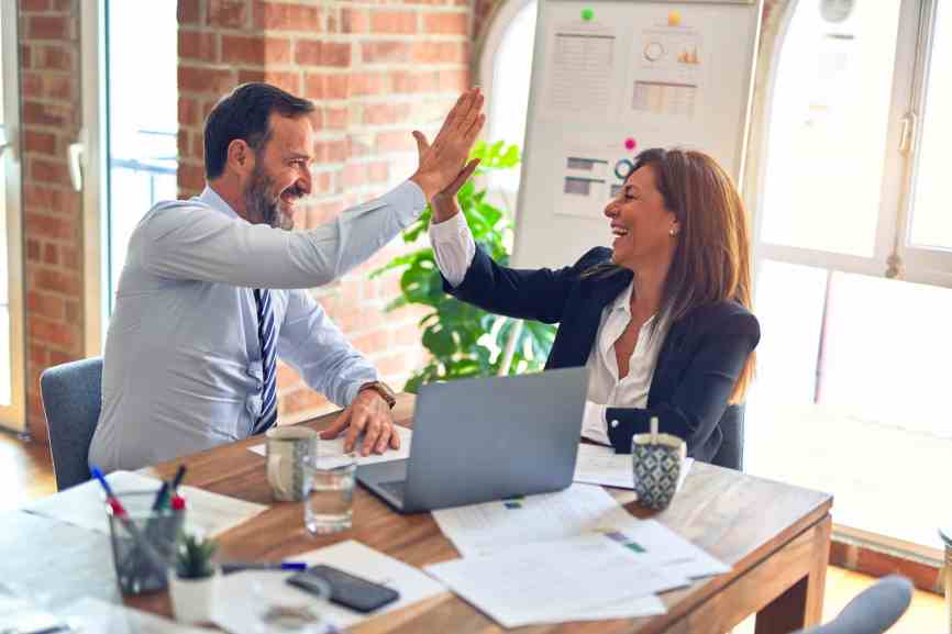A man and a woman sitting at a work table high-fiving and laughing